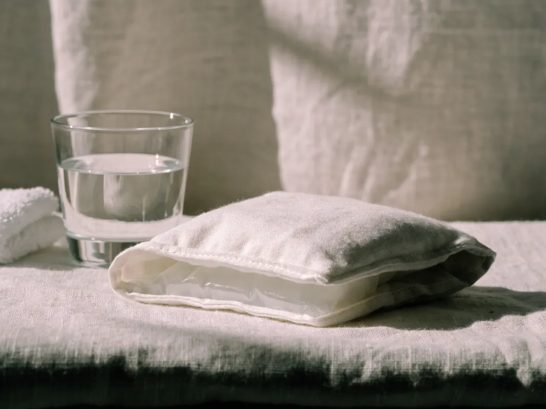 Cold compress folded in a cotton sleeve beside a glass of water for post-surgery swelling care