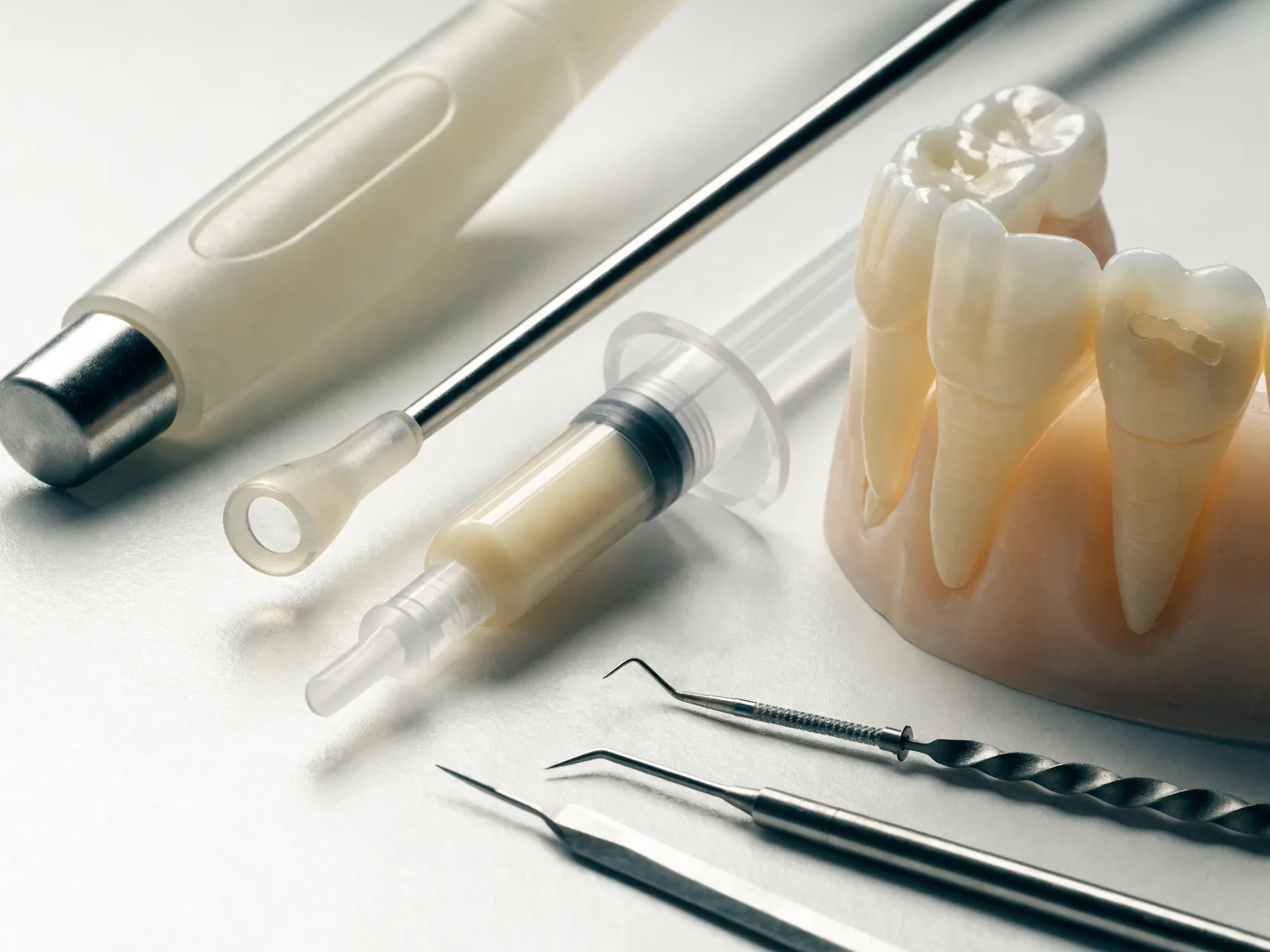 Composite bonding materials, curing light and shaping instruments beside a model of upper front teeth