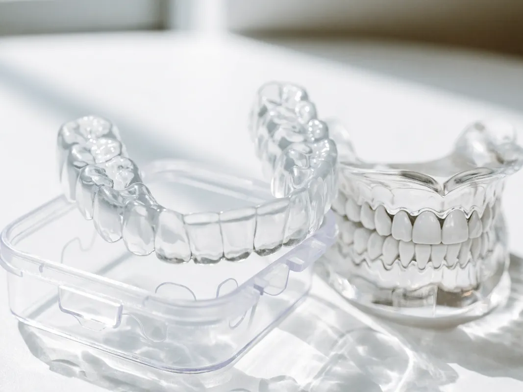Clear thermoformed night guard resting on its case beside a dental arch model
