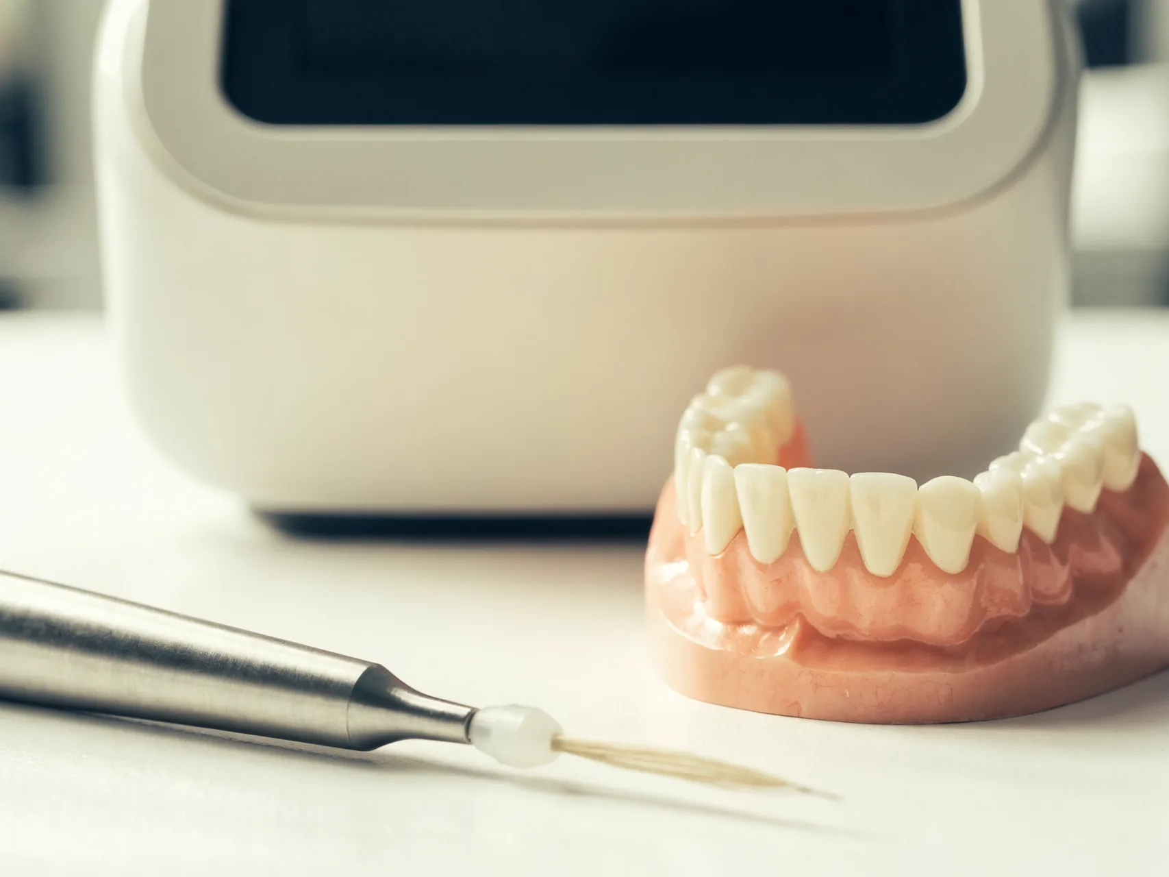 Soft-tissue dental laser handpiece beside a model of the upper gums