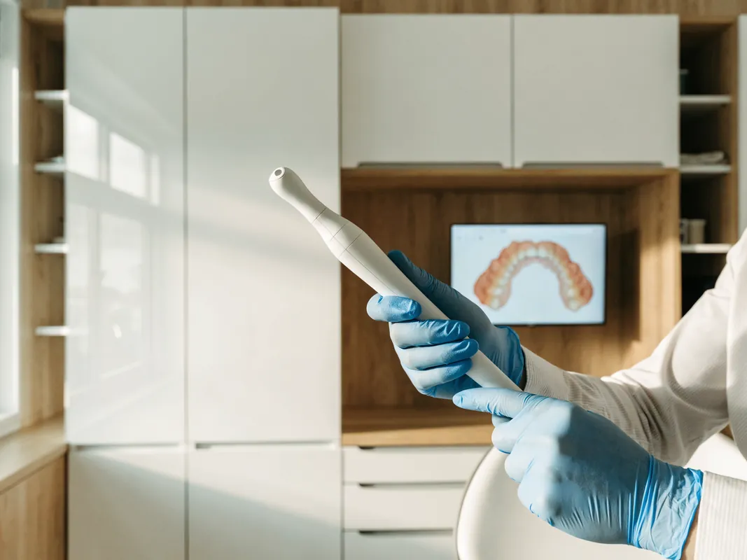 Behandler führt einen digitalen Intraoralscanner, im Hintergrund der dreidimensionale Scan des Kiefers auf dem Bildschirm